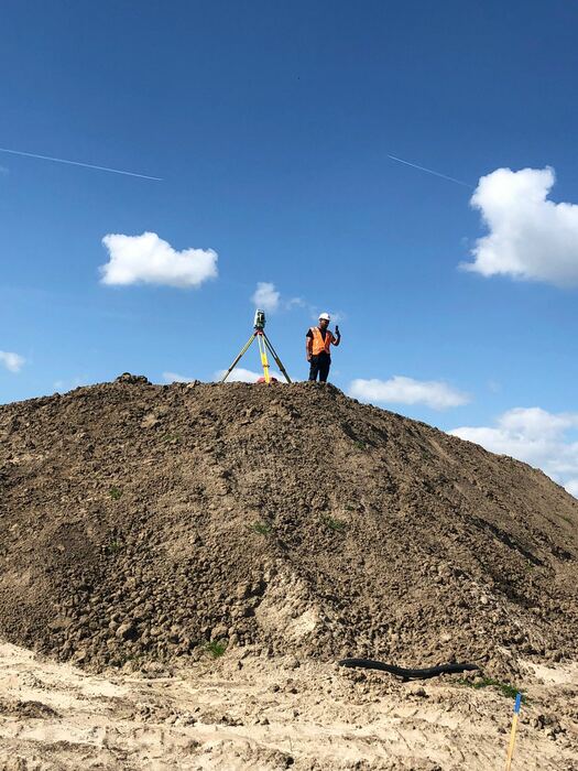 Landmeter met GPS-meetstok boven op een grondhoop