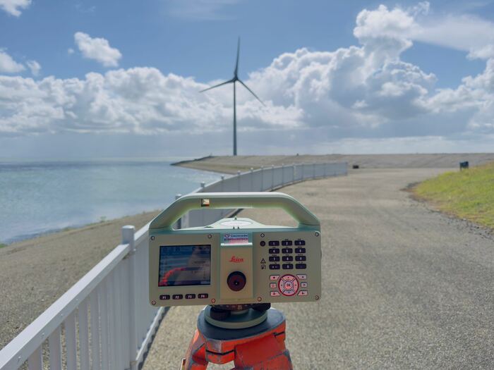 Totalstation op een zeedijk met windturbine op de achtergrond