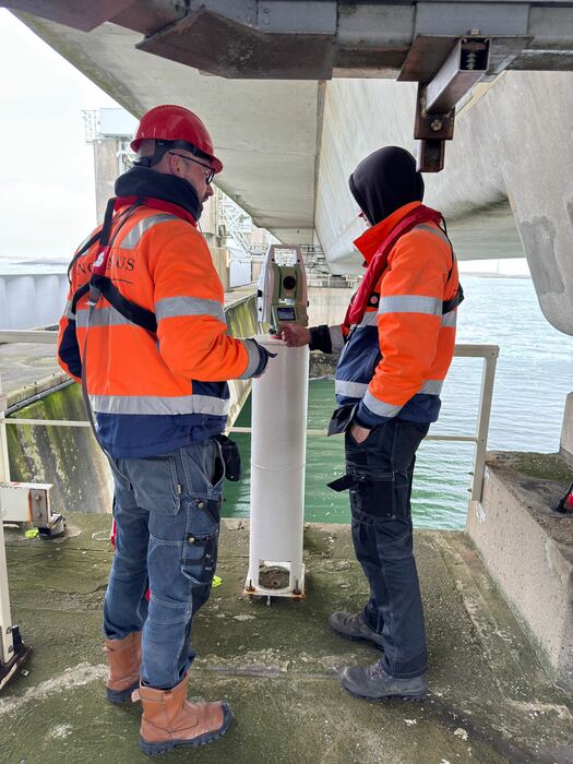 Twee landmeters werken met meetapparatuur onder een brugdek