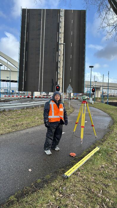 Landmeter loopt met statief naar een hefbrug