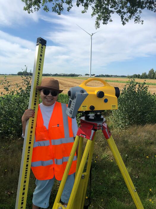 Landmeter met waterpasinstrument en baak in een weiland