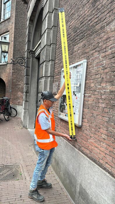 Landmeter meet met baak langs de gevel van een monumentaal pand