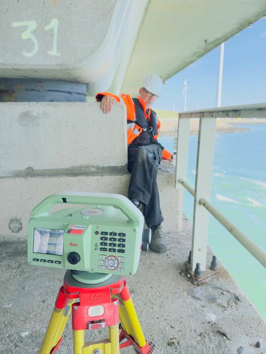 Landmeter wijst een meetpunt aan op een betonnen pijler