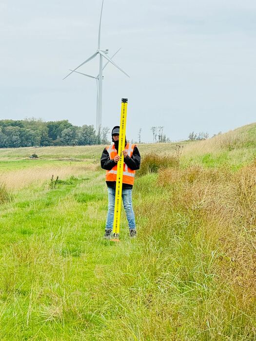 Landmeter met meetstok in een weiland bij een windturbine