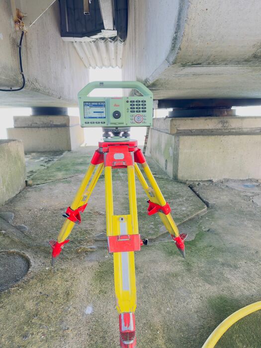 Totalstation op geel statief onder een betonnen kunstwerk