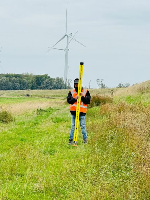 Landmeter met meetstok langs een dijk